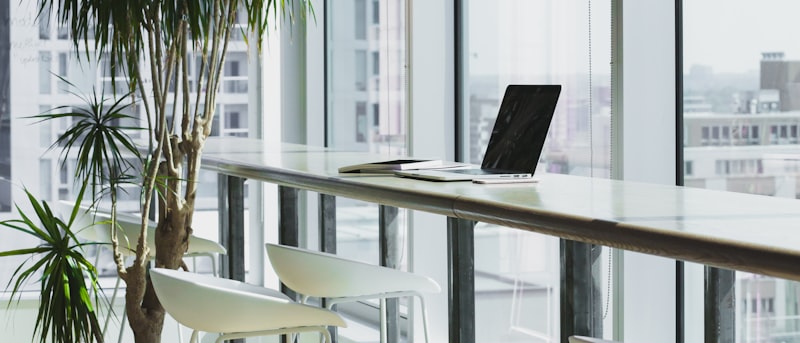 A laptop on a bar-height desk beside a tall window