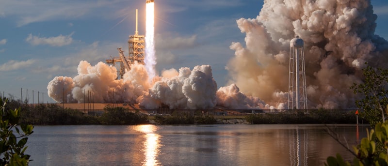 A rocket lifting off above the water, trailing exhaust