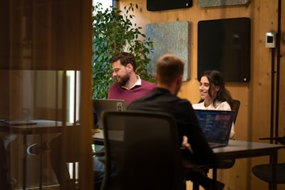 Three colleagues talking over laptops in a small room